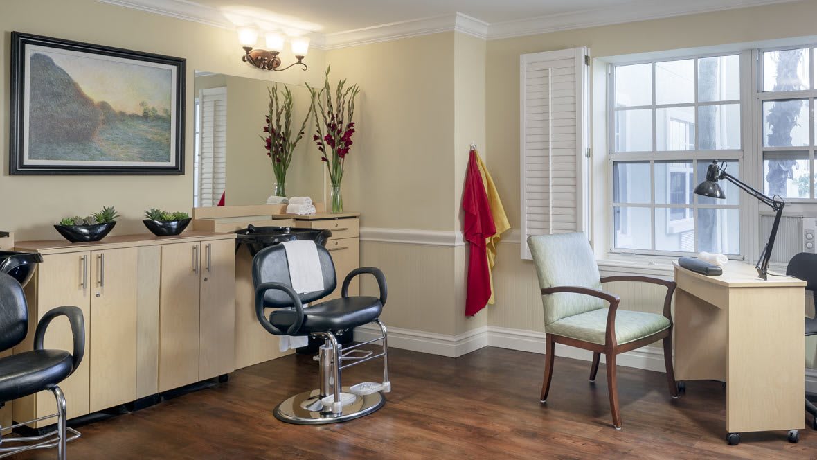 A cozy salon interior with a barber chair, mirror, and decorative flowers by the window.