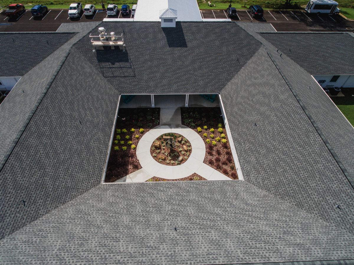Aerial view of a building with a central courtyard surrounded by a gray shingled roof.