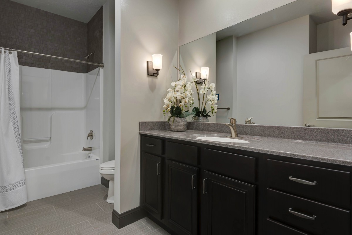 A modern bathroom with dark cabinets, a large mirror, and floral decor.