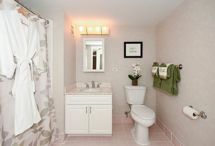 A clean and modern bathroom featuring a sink, toilet, and shower with green towels as decor.