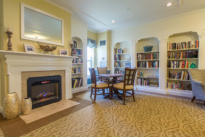 A cozy living room with a fireplace, surrounded by built-in bookshelves and a round table with chairs.