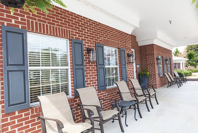 A brick porch with lined-up chairs and windows.