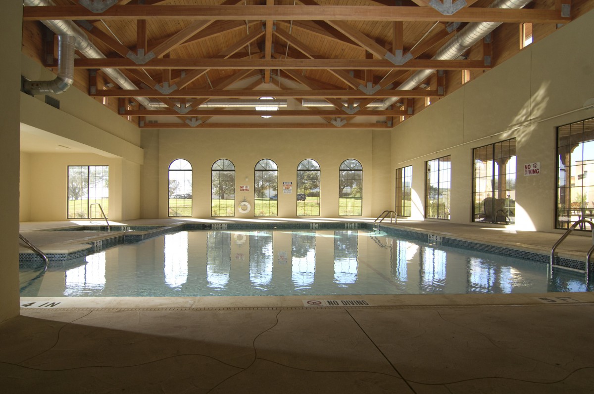 A serene indoor swimming pool with wooden beam architecture and large windows.