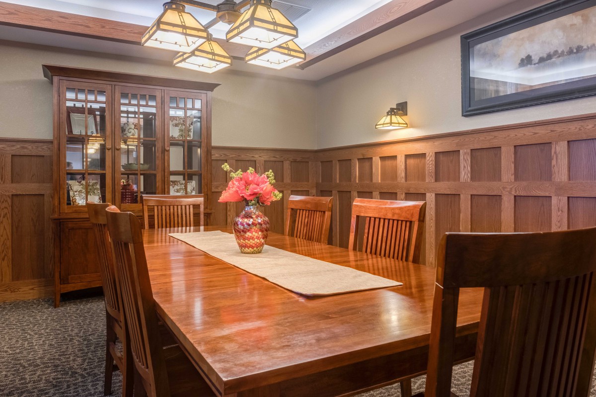 A warmly lit dining room featuring a wooden table with chairs, highlighted by a floral centerpiece and elegant lighting.