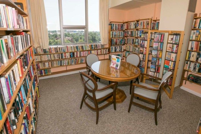 A cozy library corner with bookshelves, a round table, and chairs by the window.
