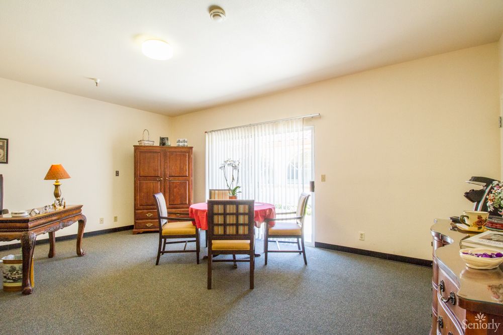 A dining room with a table and four chairs, featuring a large window and a wooden cabinet.