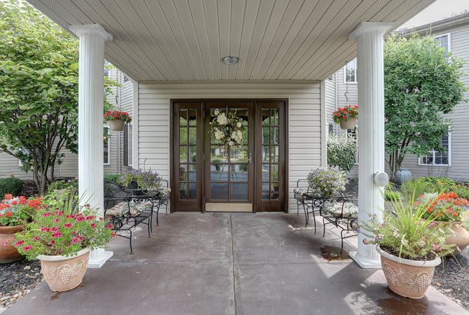 A welcoming porch with columns, decorated with potted flowers and seating.