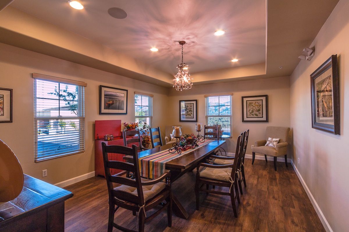 A cozy, traditional-style dining room with a chandelier and wooden flooring, illuminated by natural light from the surrounding windows.
