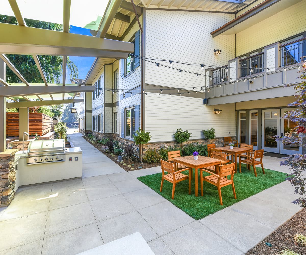 A modern courtyard featuring tables and chairs, enhanced by string lights and landscaping.