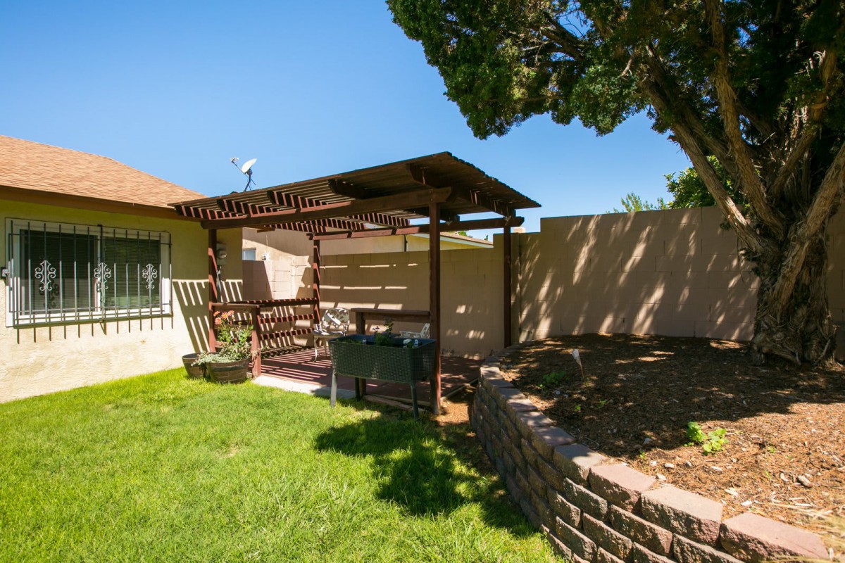 A sunny backyard with a pergola and outdoor seating area on a neatly maintained lawn.