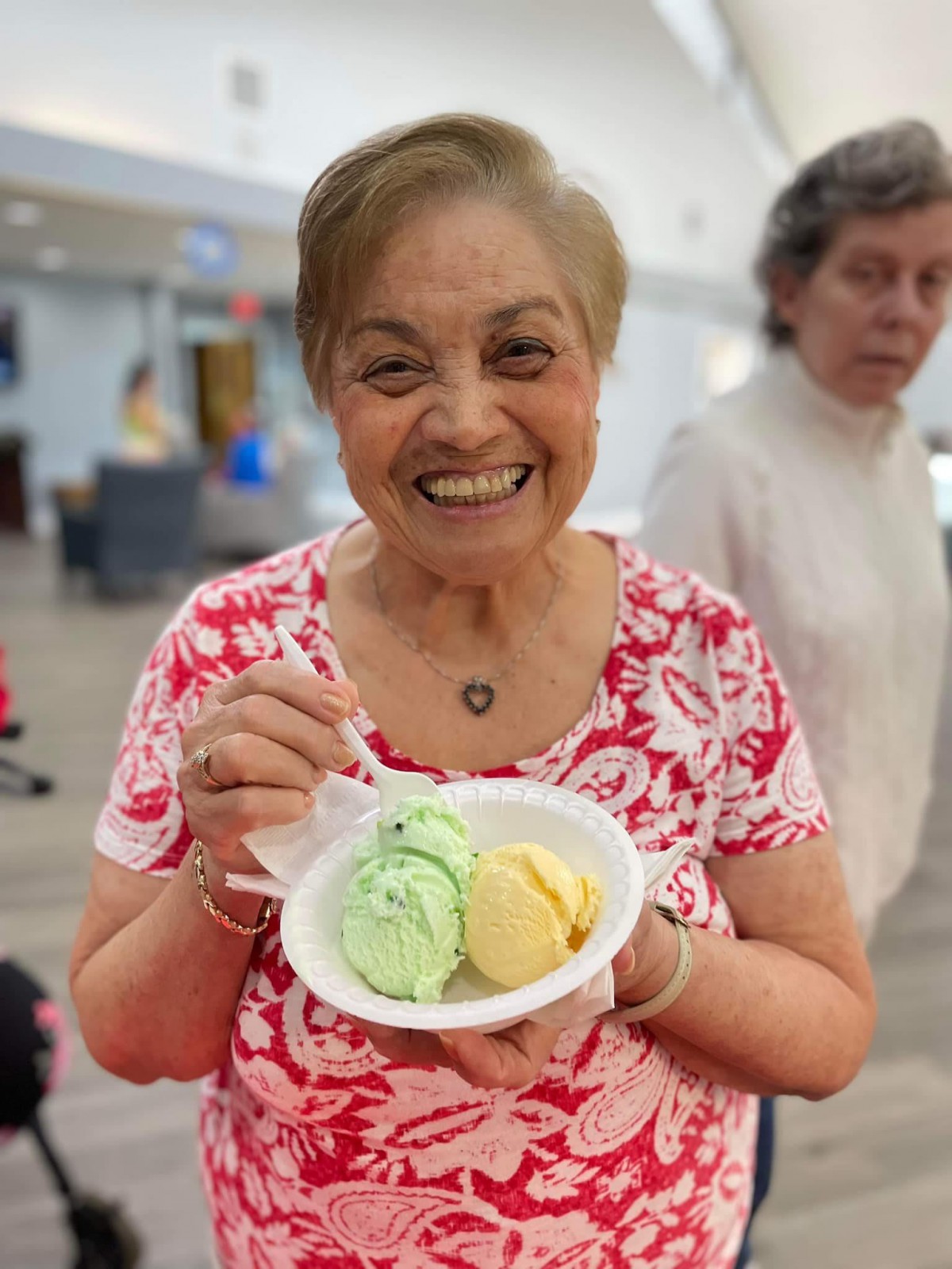 A woman happily holding a bowl of colorful ice cream indoors.
