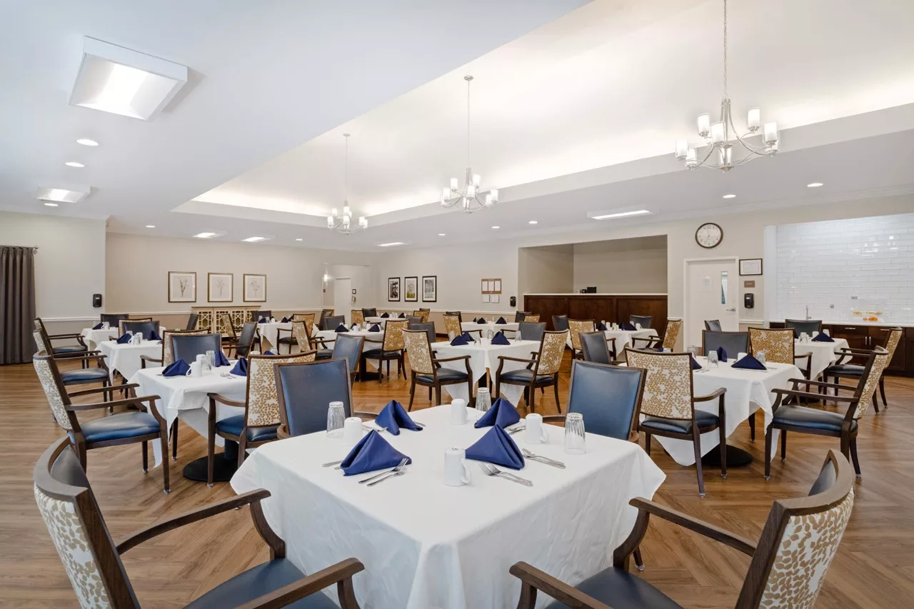 An elegantly set dining room with neatly arranged tables and chairs, featuring blue napkins and soft lighting.
