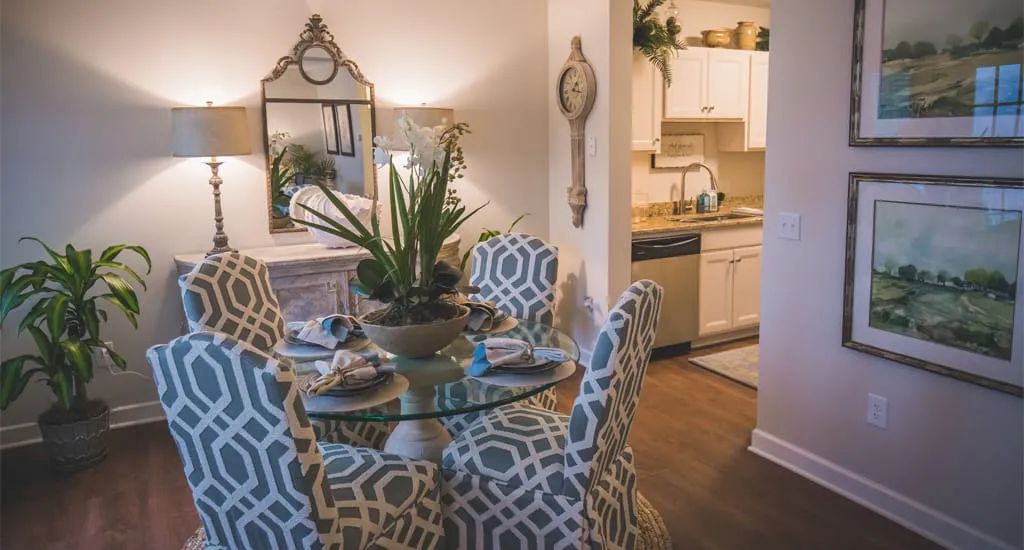 A stylish dining area with a glass round table and patterned chairs, adjacent to a kitchen.