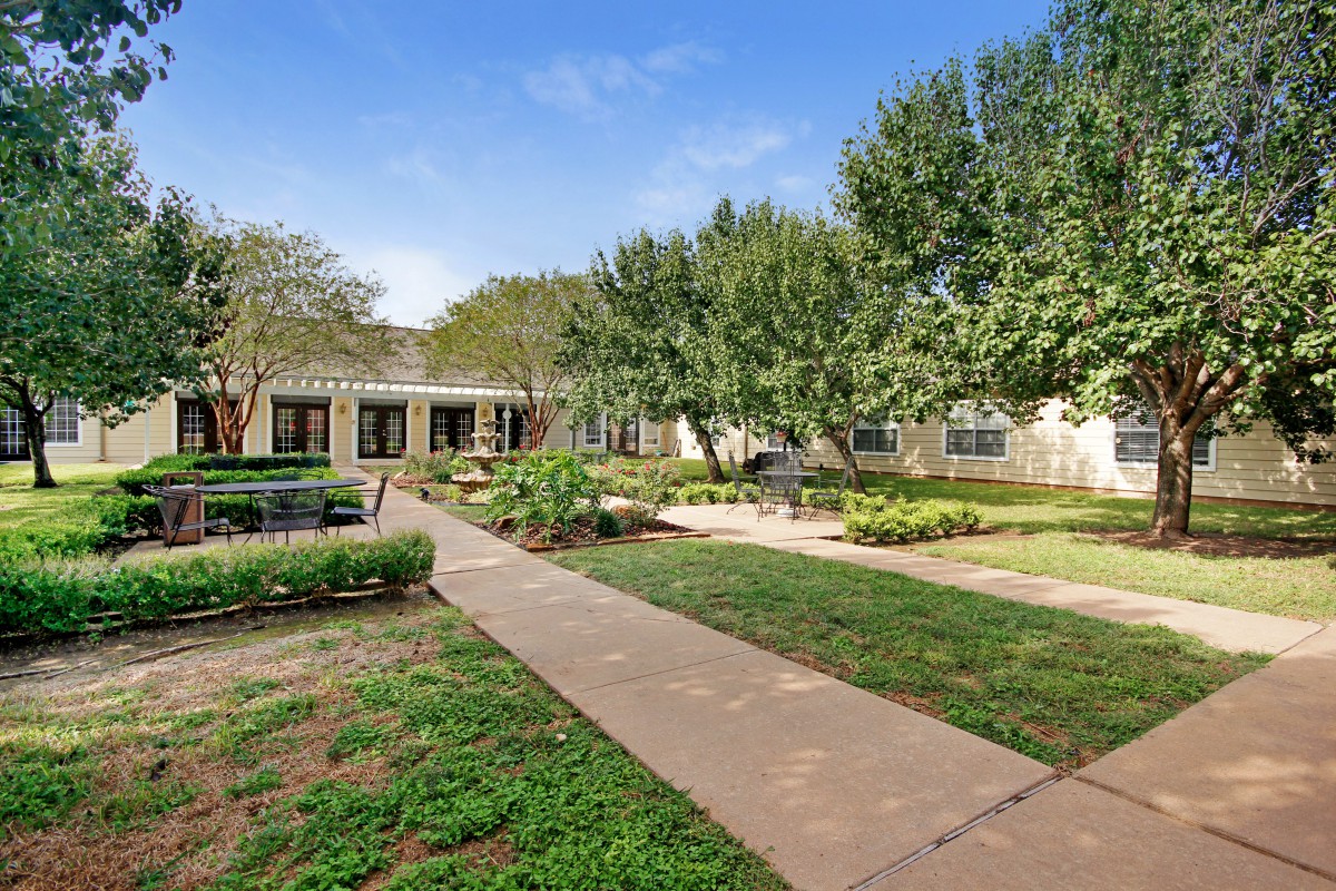 A peaceful garden with a pathway surrounded by trees and a building in the background.