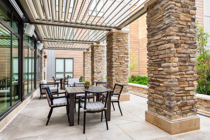 A modern outdoor patio with a pergola and stone pillars, featuring a dining table and chairs.