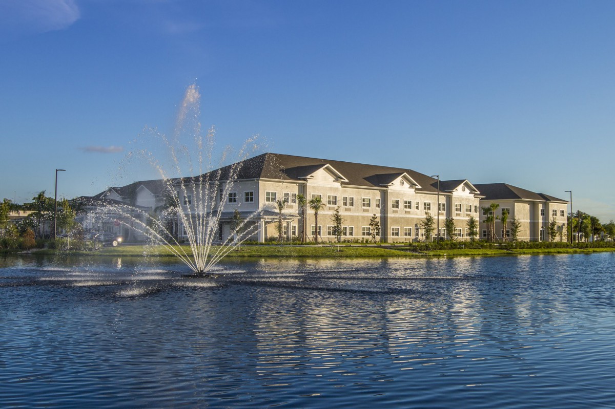 A picturesque view of a residential building with a fountain in a pond during the daytime.