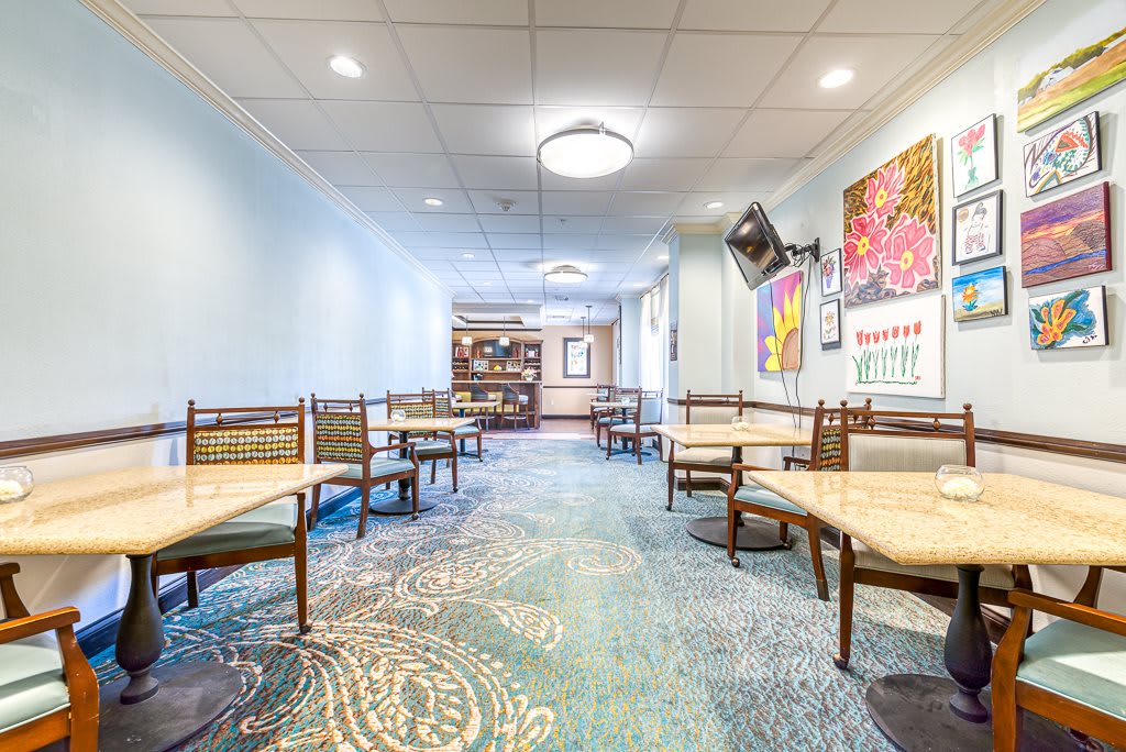 An empty dining area with tables and chairs, adorned with colorful wall art and bright lighting.