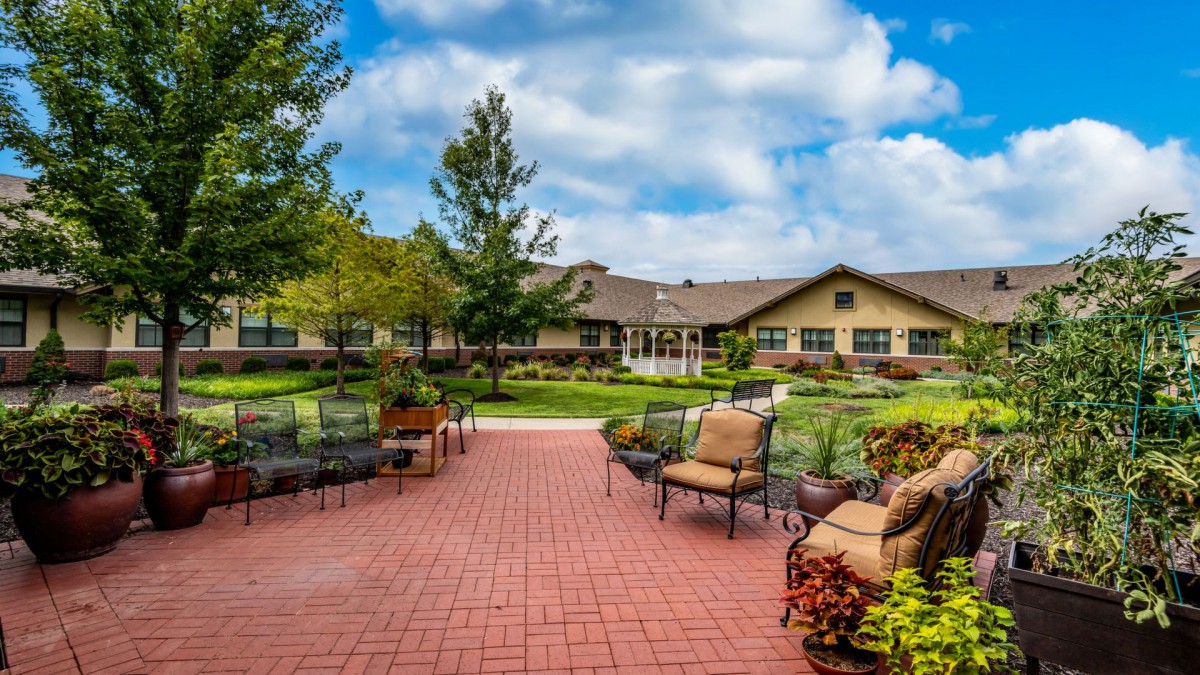 A spacious patio area with outdoor furniture, surrounded by well-maintained gardens and a large building in the background.