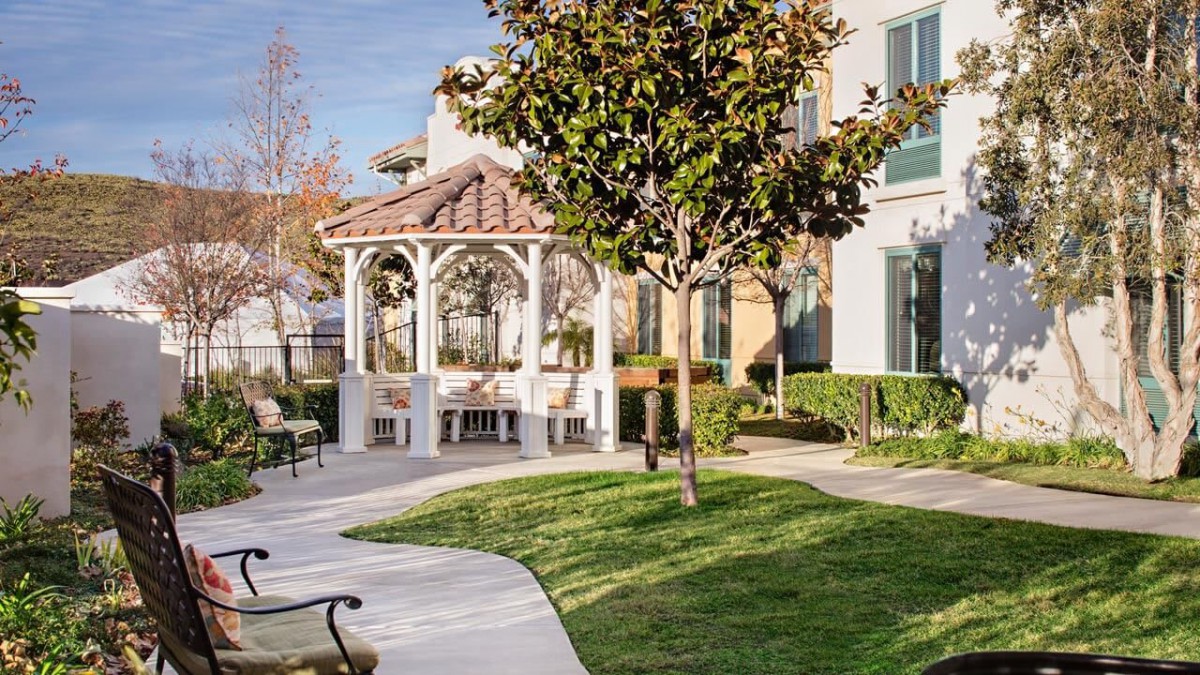 A serene garden featuring a white gazebo, surrounded by lush greenery and a winding pathway.