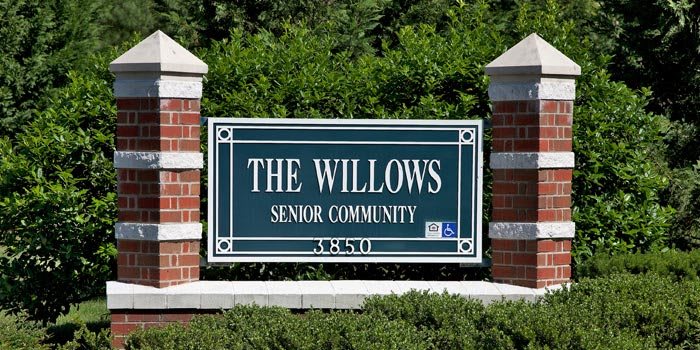 Sign for The Willows Senior Community surrounded by greenery and brick pillars.