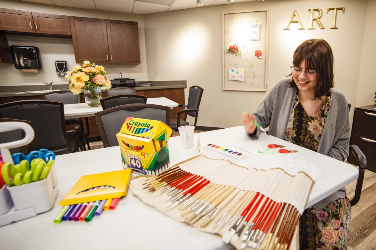 A person engaged in a creative activity, surrounded by crayons and markers at a table.
