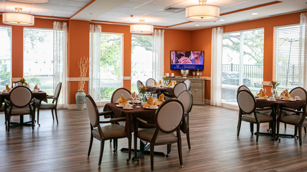 A cozy dining area with neatly arranged tables, an orange accent wall, and a television.