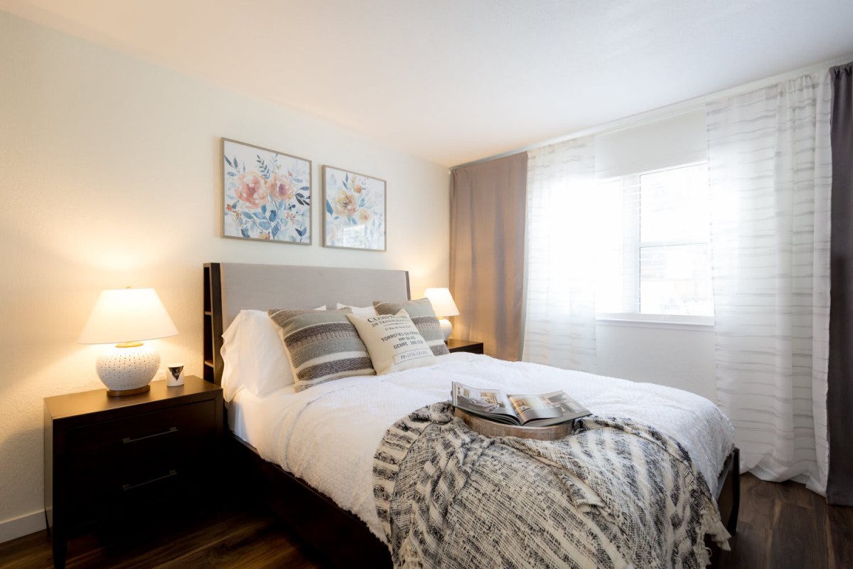 A cozy and modern bedroom with stylish decor, featuring a comfortable bed, artwork above the headboard, and soft lighting.