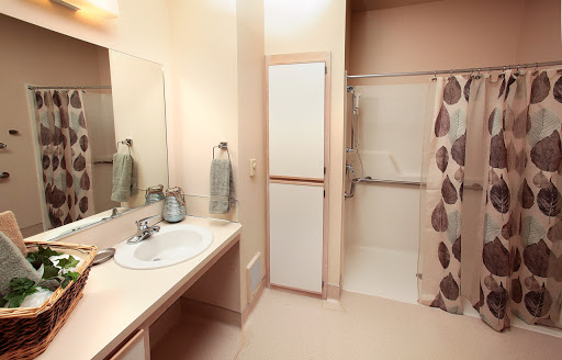 A well-lit bathroom featuring a shower, sink, mirror, and storage cabinets.
