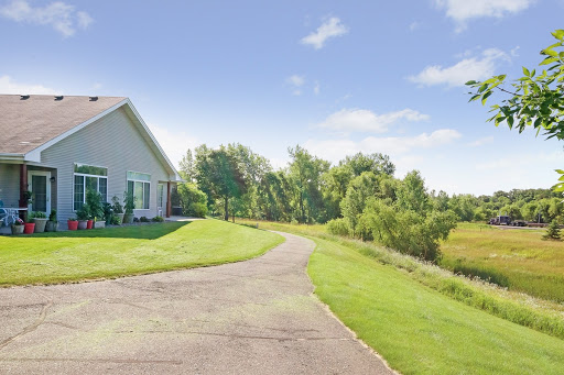 A serene view of a house with a winding driveway surrounded by lush greenery and a clear blue sky.