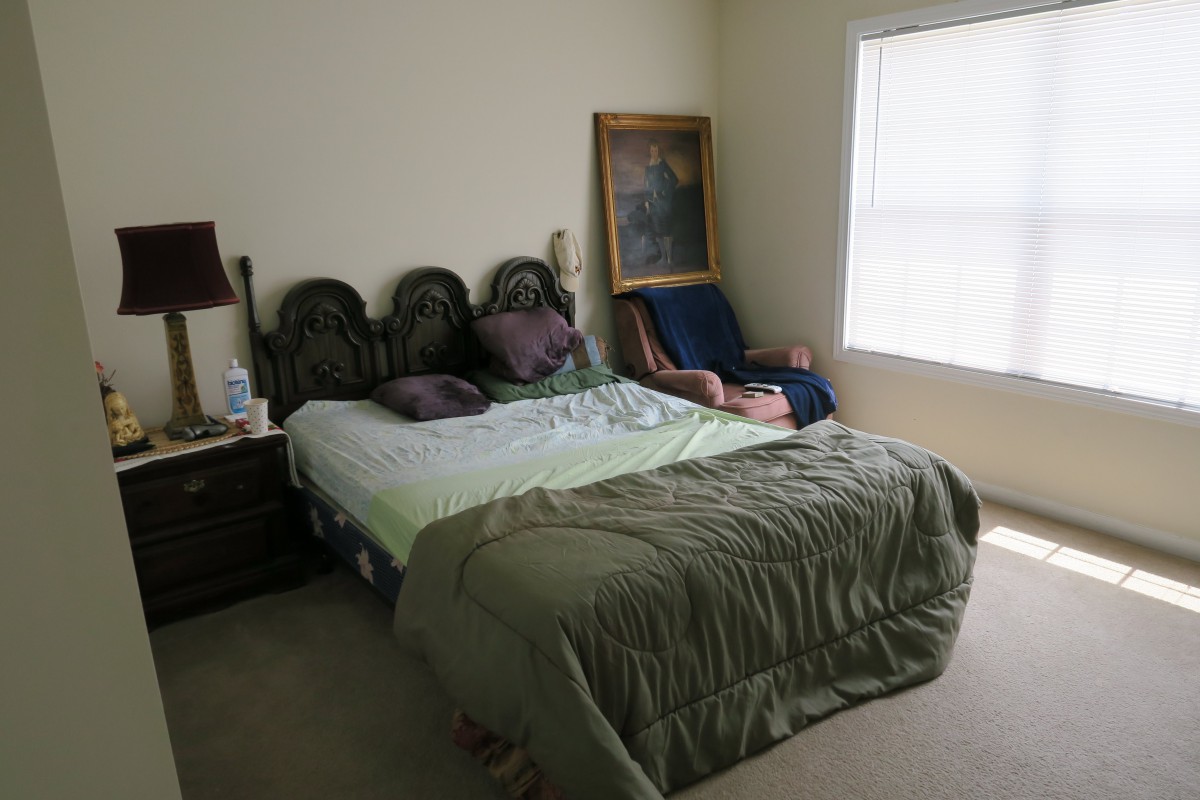 A bedroom with a bed, a painting propped up against the wall, and a chair by the window.