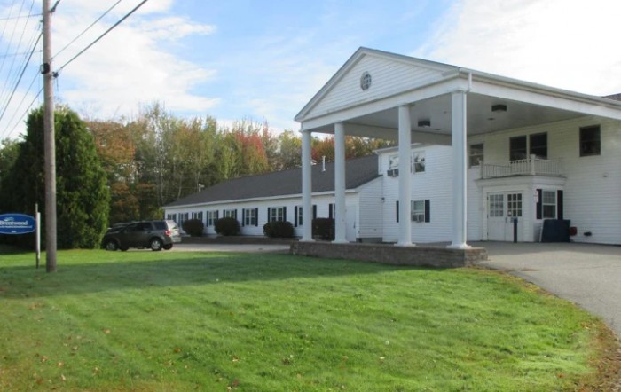 A white building with columns, surrounded by green grass and trees.