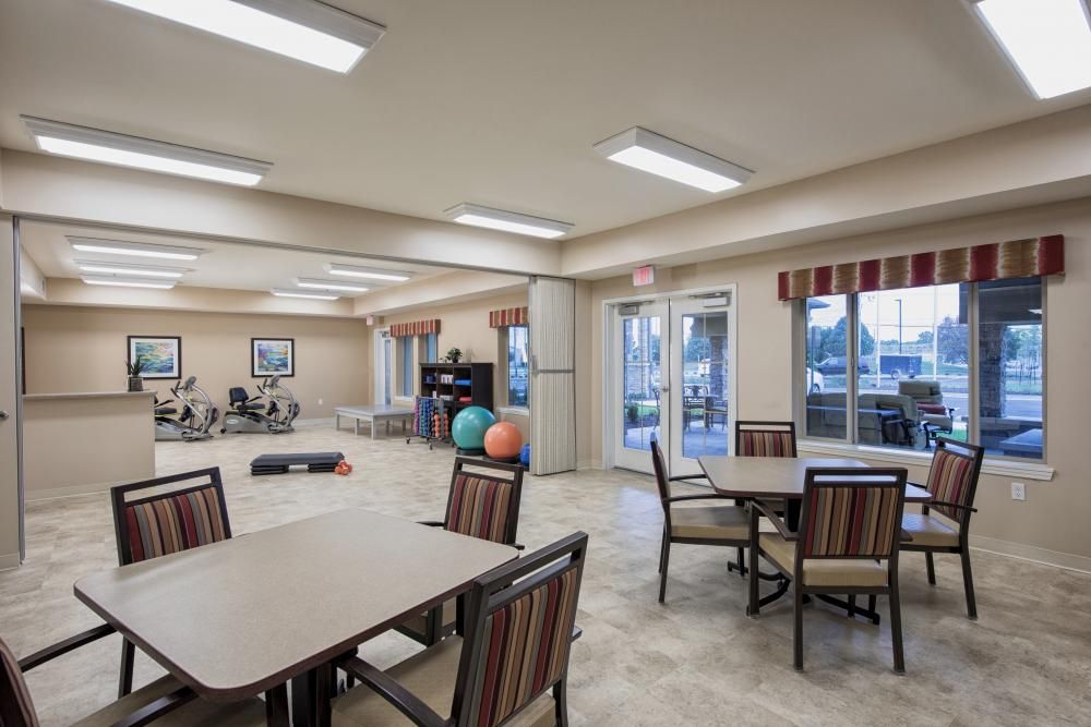 A well-lit community room with tables, chairs, and exercise equipment.
