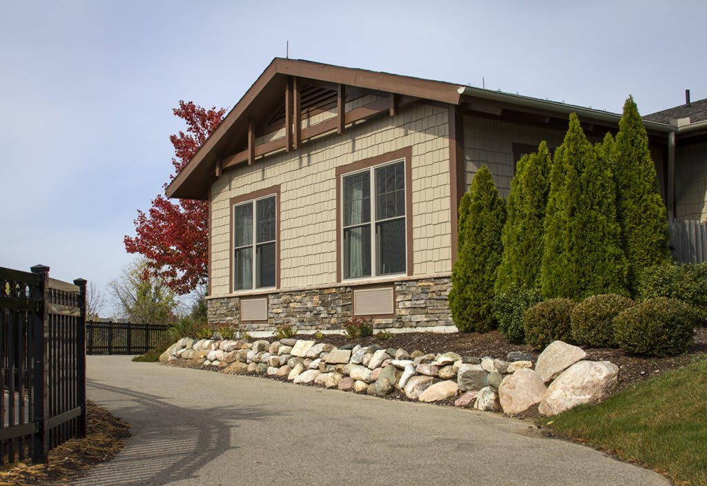 A modern house with stone siding, surrounded by lush greenery and a clear sky.
