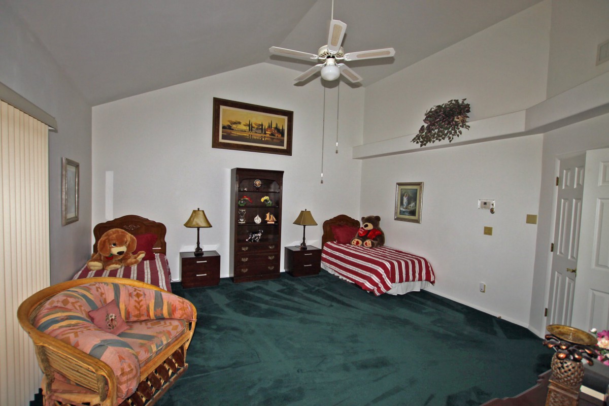 A spacious bedroom with twin beds, decorated with a ceiling fan and wall art.