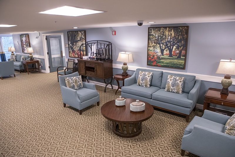 A cozy living room with blue sofas, an armchair, a wooden coffee table, and decorative paintings.