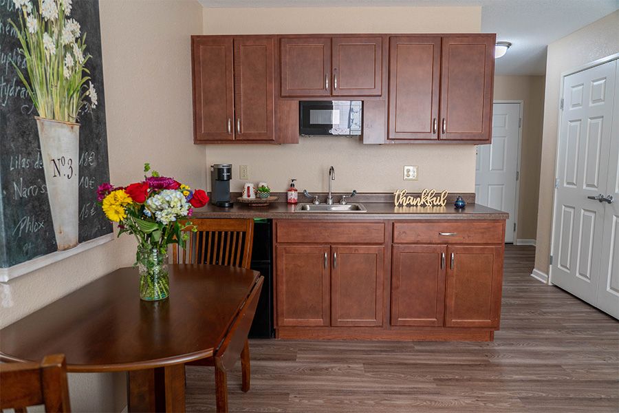 A cozy kitchen area with wooden cabinets, a small dining table with flowers, and modern appliances.
