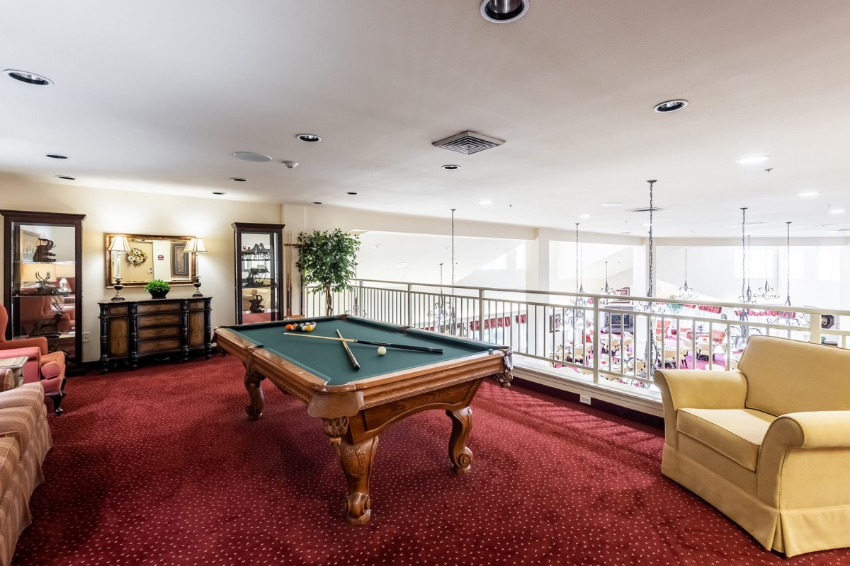 A spacious game room with a pool table and cozy seating area on red carpet flooring.