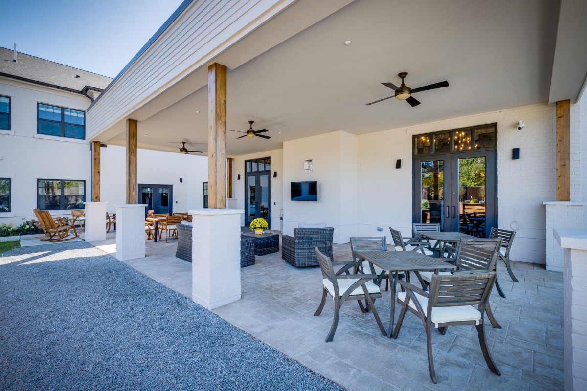 A modern outdoor patio with comfortable seating and dining area, featuring ceiling fans for added comfort.