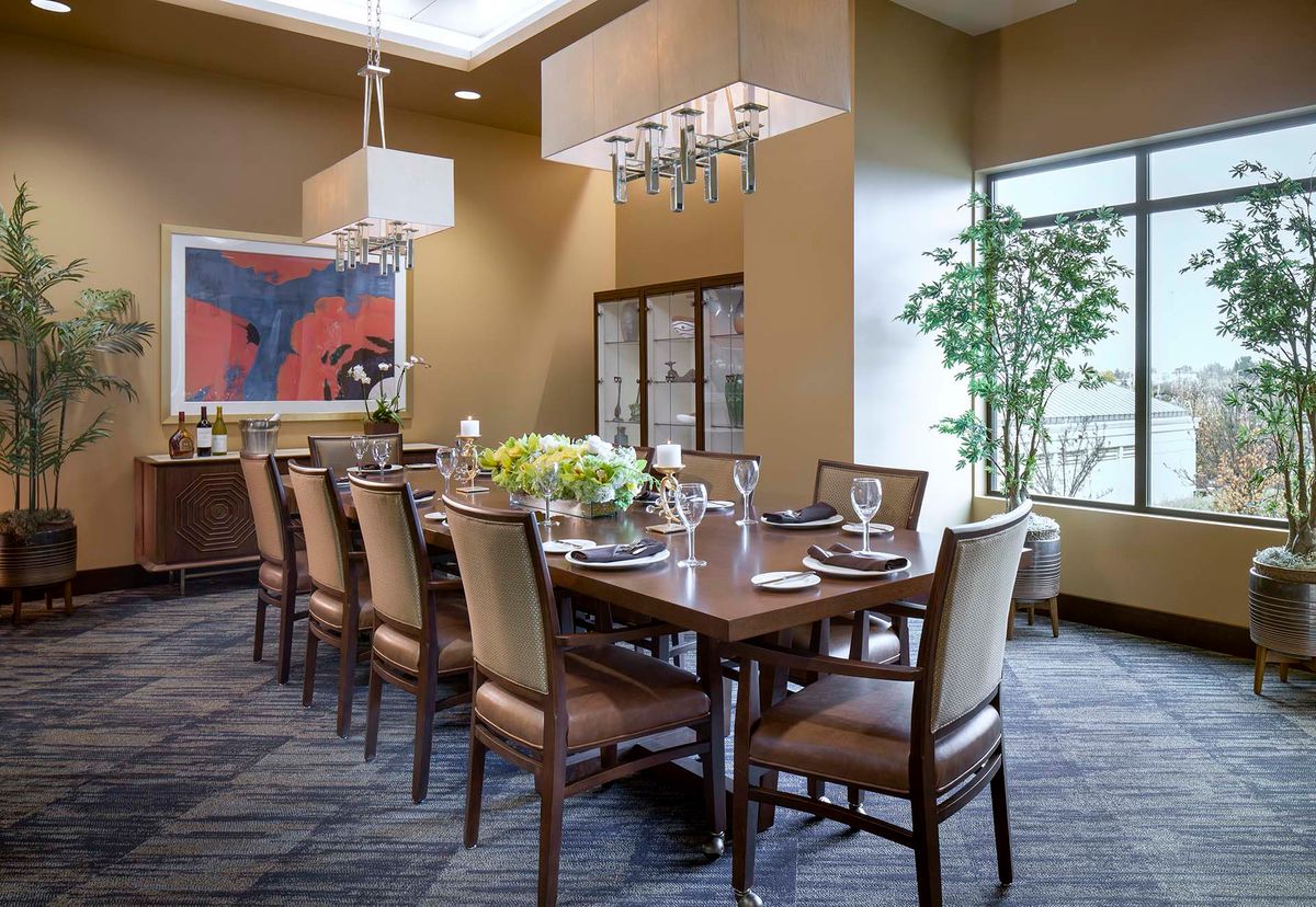 A well-appointed dining room with a long wooden table set for a formal meal, featuring elegant chairs, chandeliers, and contemporary artwork.