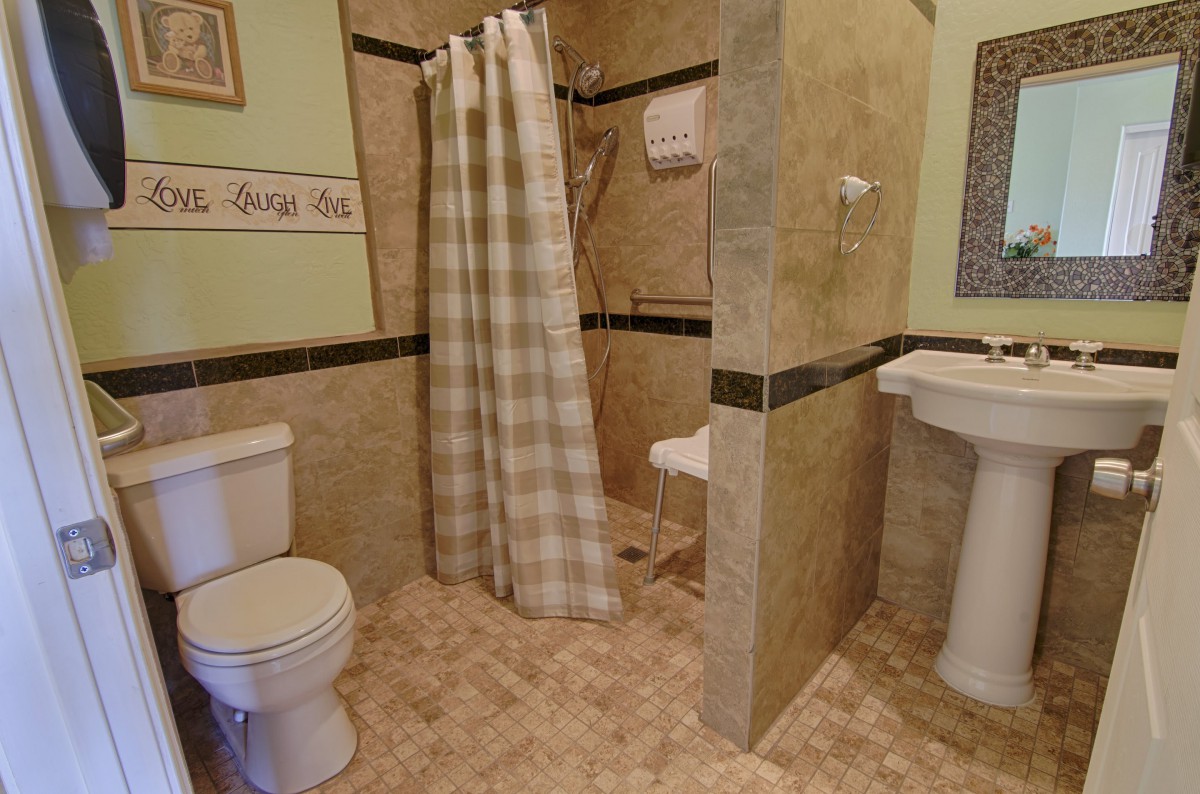 A modern bathroom featuring a shower with a checked curtain, toilet, and pedestal sink.