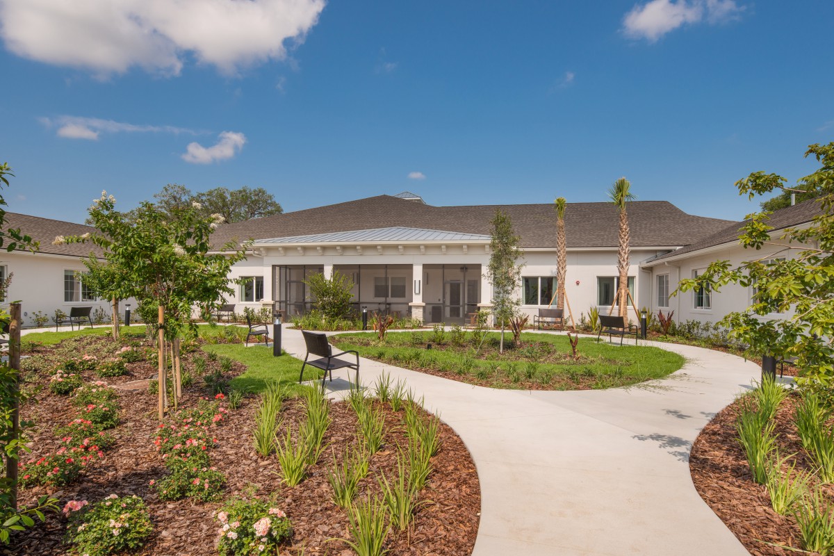 A modern building with a landscaped garden and winding pathway under a blue sky.