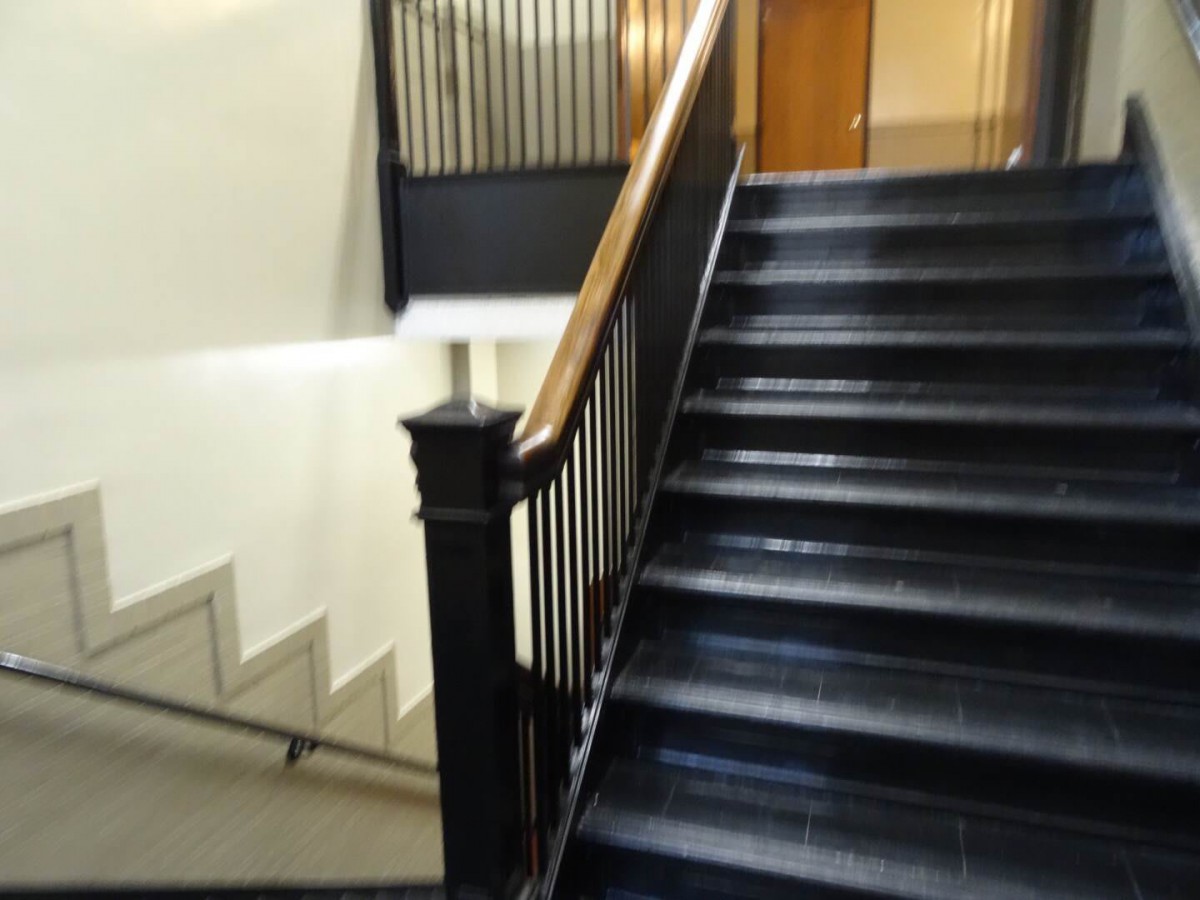 A view of an interior staircase with metal railings and a wooden handrail.