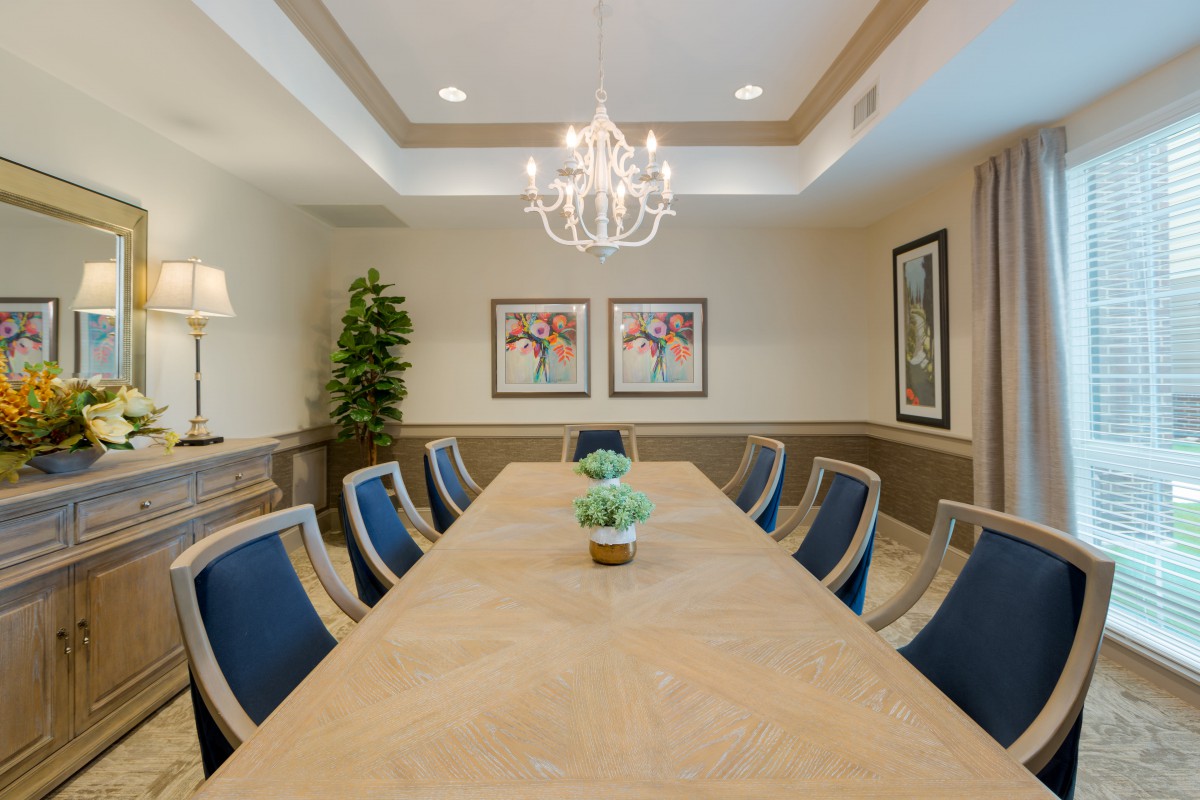 A well-lit conference room featuring a large meeting table surrounded by chairs, with a chandelier overhead and decorative artwork on the walls.