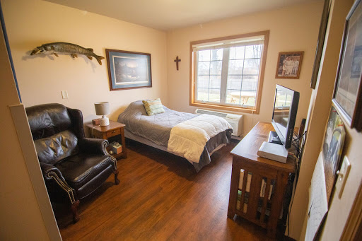 A cozy bedroom featuring a comfortable bed, a chair, and a television, illuminated by natural light from the window.