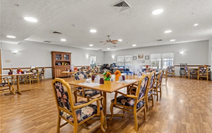 A bright and spacious dining room with neatly arranged tables and chairs, featuring a wooden floor and decorative elements.