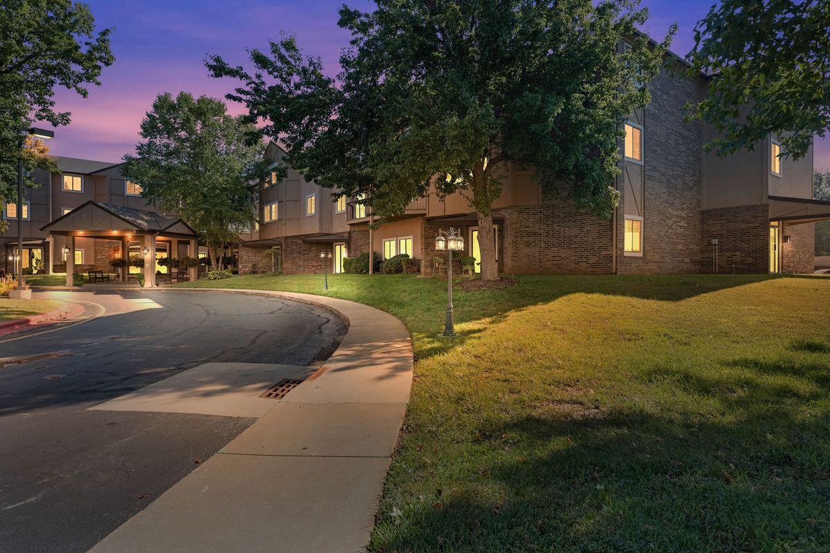 A well-lit building at dusk with a pathway and surrounding trees.
