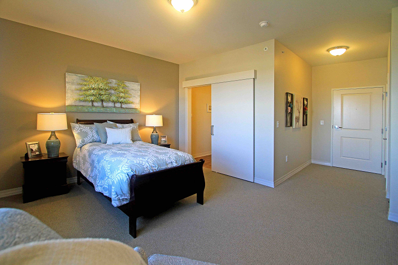 A cozy bedroom with a neatly made bed, side lamp, and wall art.