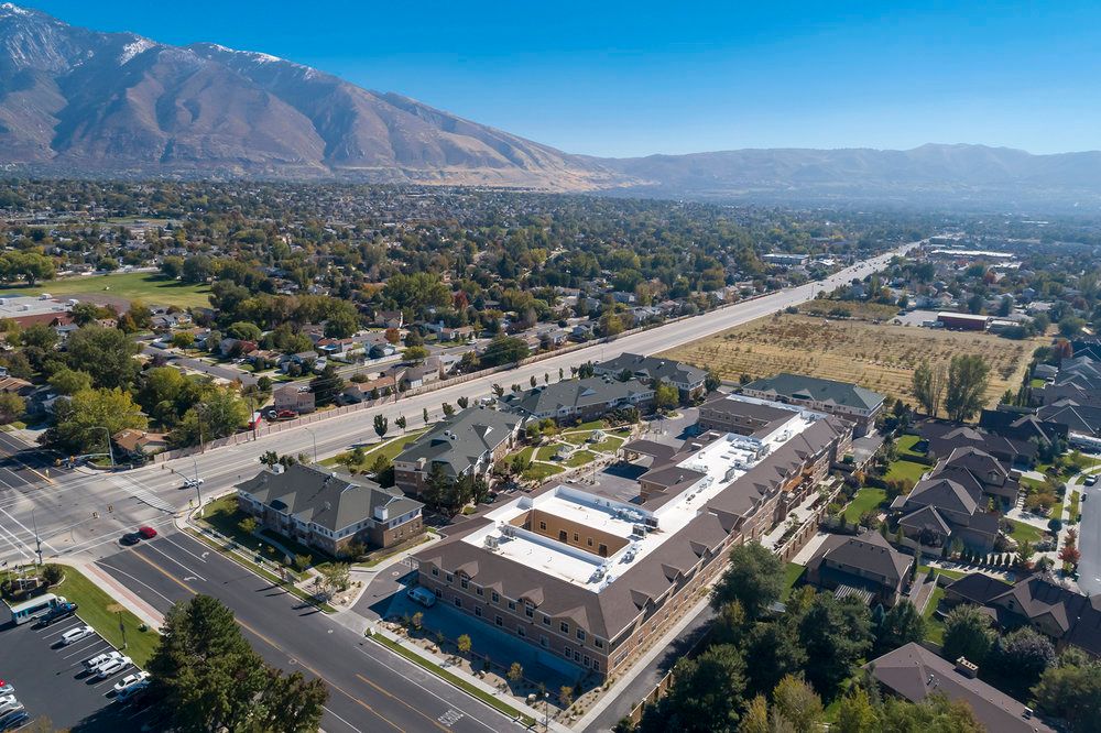 Aerial view of a suburban neighborhood with buildings and a road, set against a backdrop of mountains.