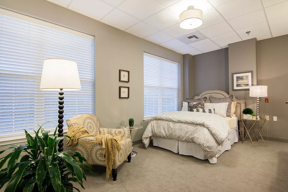 A cozy bedroom with neutral tones, featuring a comfortable bed, an upholstered chair, and a floor lamp.