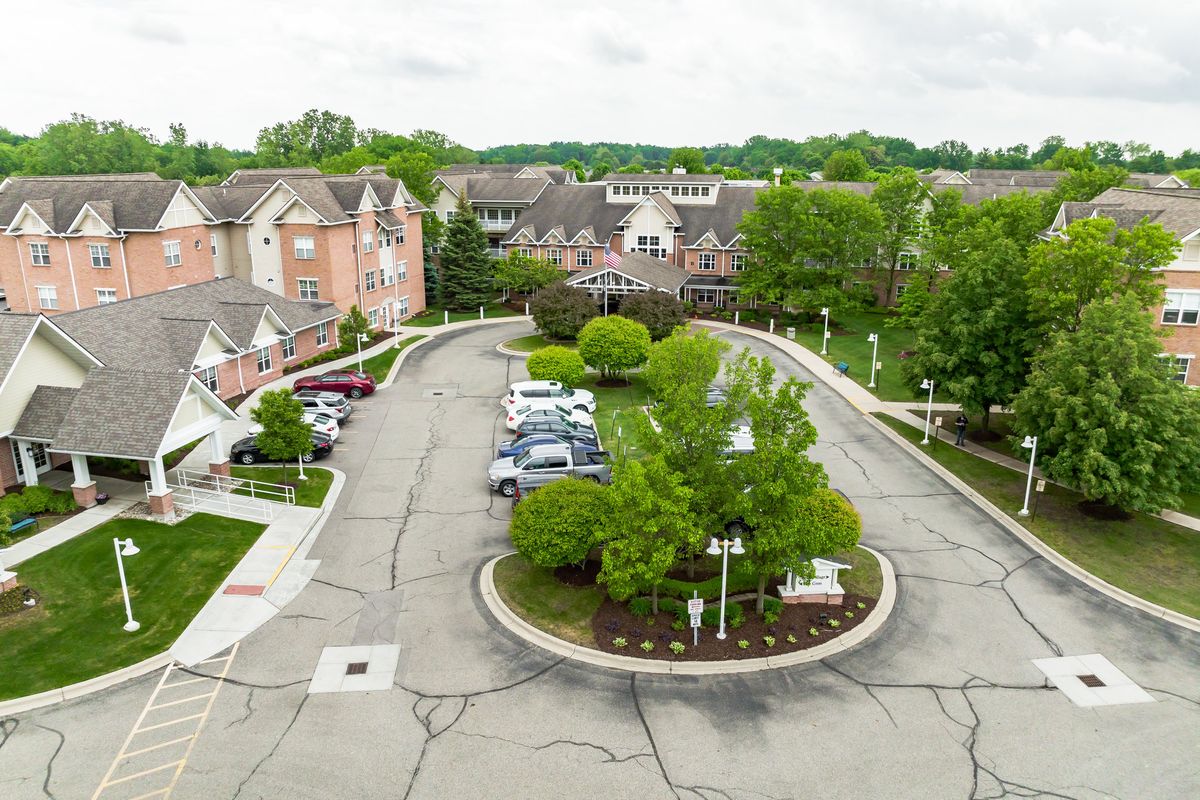 Aerial view of a residential complex with surrounding greenery and parked cars.